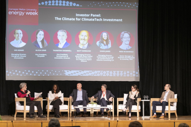 Six people sit on a stage as a panel